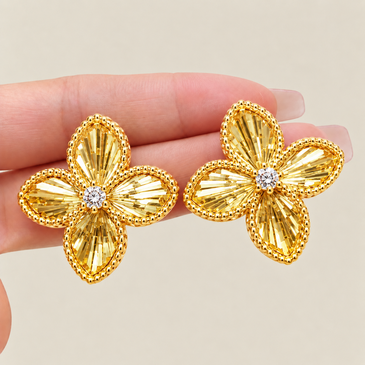 Gold-tone four-petal flower stud earrings shown by hand