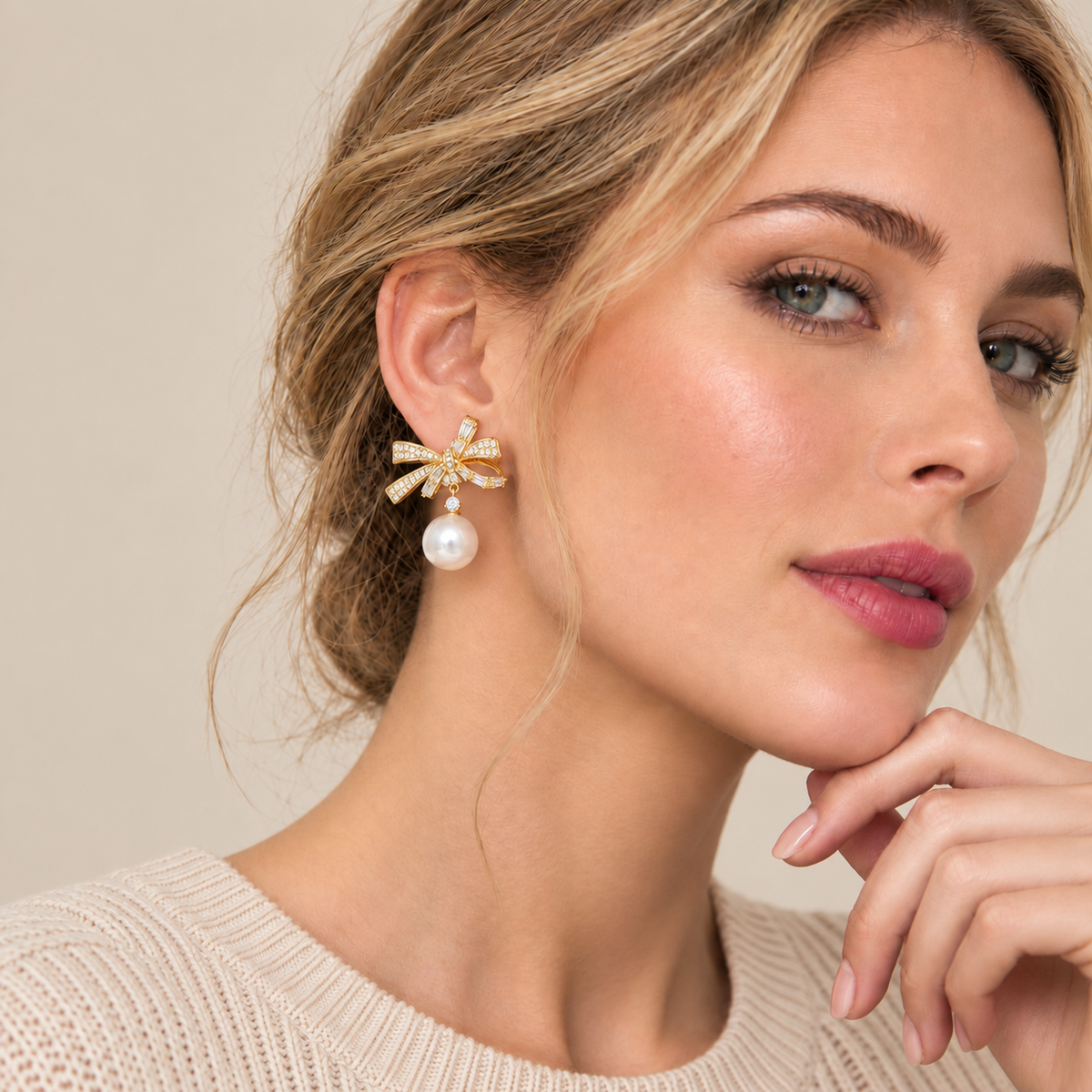 Model wearing gold-tone rhinestone bow earrings with faux pearl drops