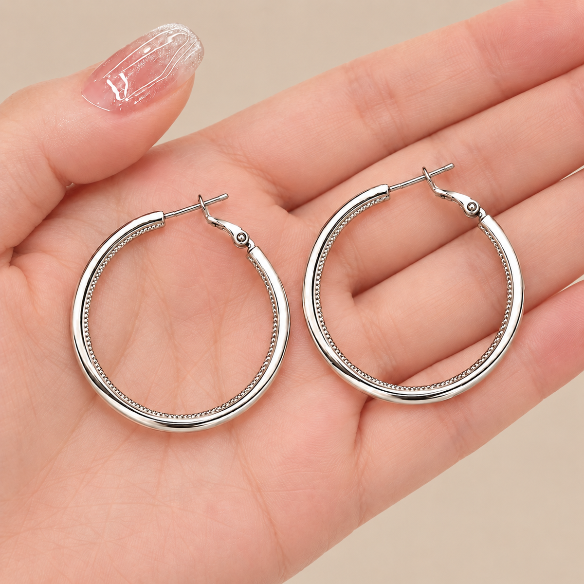 Silver hoop earrings displayed in hand showing textured inner detail